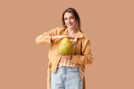 Mujer joven sonriente con pomelo sobre fondo marrón