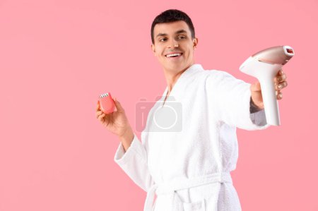 Junger Mann mit verschiedenen Epilatoren auf rosa Hintergrund