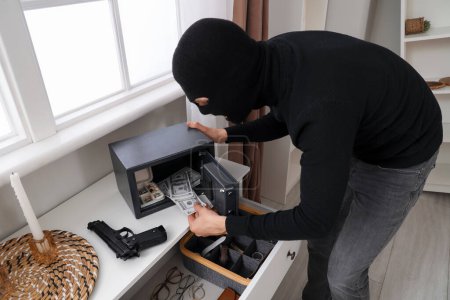 Male thief stealing money from safe in room