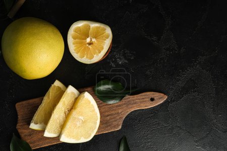 Foto de Tablero de madera con trozos de pomelo fresco sobre fondo negro - Imagen libre de derechos