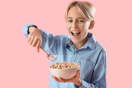 Joyeux petit garçon mangeant des anneaux de céréales sur fond rose