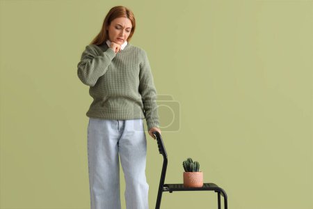 Mature woman with hemorrhoids and cactus on chair against green background