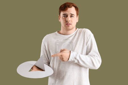Young man pointing at paper thumbtack on green background. Hemorrhoids concept