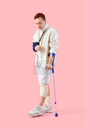 Verletzter junger Mann nach Unfall mit Krücke auf rosa Hintergrund
