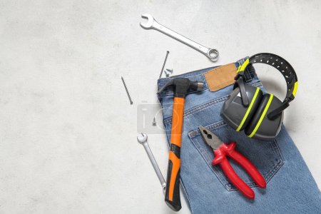 Foto de Composición con diferentes herramientas, orejeras y jeans sobre fondo blanco. Fiesta del Día del Trabajo - Imagen libre de derechos