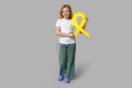 Téléchargez les photos : Adolescente avec ruban jaune sur fond gris. Journée internationale du cancer chez les enfants - en image libre de droit