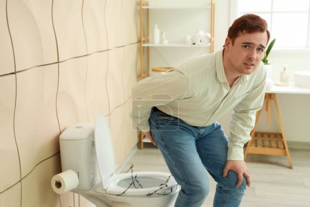 Jeune homme avec hémorroïdes et cuvette de toilette barbelée dans les toilettes
