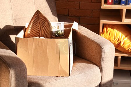 Téléchargez les photos : Boîte de choses indésirables pour la vente de garage sur fauteuil dans la chambre - en image libre de droit