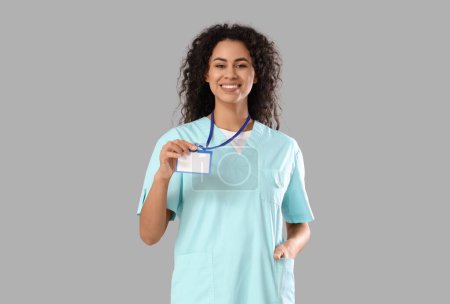Female African-American medical intern with badge on light background