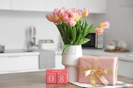 Téléchargez les photos : Calendrier avec date de la Journée internationale de la femme, boîte cadeau et tulipes sur la table dans la cuisine - en image libre de droit