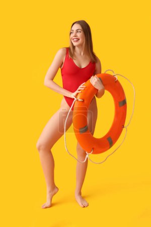Schöne junge Frau im Panzer-Badeanzug und mit Rettungsring auf gelbem Hintergrund