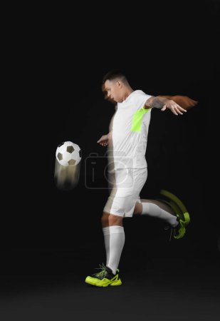 Junger Mann spielt Fußball in Bewegung auf dunklem Hintergrund