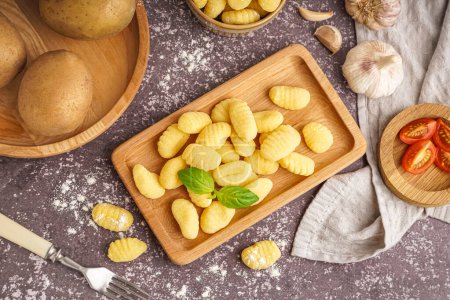 Wooden board with tasty gnocchi, tomatoes, garlic and basil on grunge background