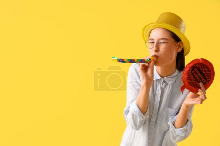 Geschäftsfrau mit Party-Gebläse und Kaugummikissen auf gelbem Hintergrund. Feier zum Aprilscherz