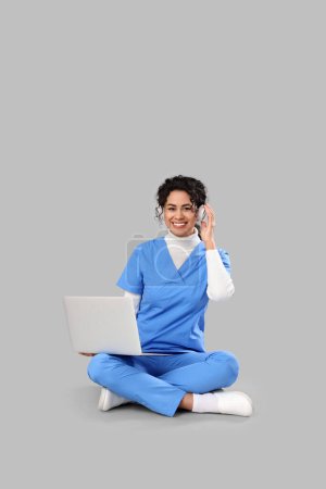 Pasante médica afroamericana en auriculares con portátil sobre fondo claro