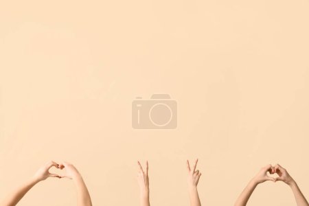 Téléchargez les photos : Mains féminines montrant la paix et les gestes du cœur sur fond beige - en image libre de droit