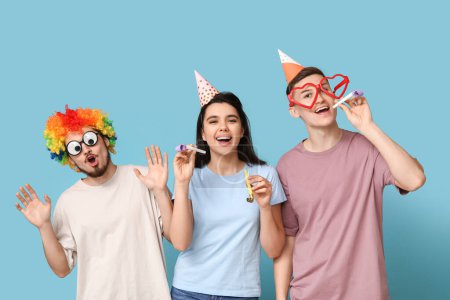 Junge Freunde in lustiger Verkleidung mit Party-Trillerpfeifen auf blauem Hintergrund. Aprilscherz-Feier