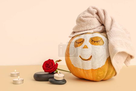 Foto de Calabazas con caras dibujadas, piedras de spa, rosa y máscara de arcilla sobre fondo beige - Imagen libre de derechos