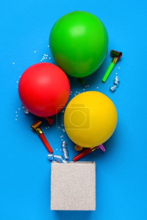 Téléchargez les photos : Boîte avec ballons, confettis et bruyants sur fond bleu - en image libre de droit