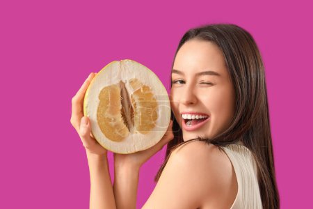 Mujer joven sonriente con la mitad de pomelo sobre fondo morado, primer plano