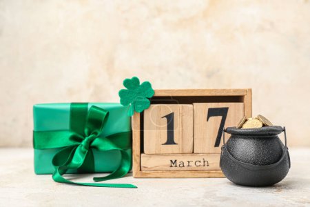 Photo for Leprechaun pot with golden coins, gift box and wooden calendar on beige grunge background. St. Patrick's Day celebration - Royalty Free Image
