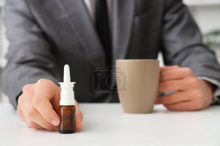 Téléchargez les photos : Homme d'affaires malade avec des gouttes nasales et une tasse de thé sur la table au bureau, gros plan - en image libre de droit
