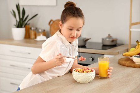 Petite fille mignonne mangeant des anneaux de céréales avec du jus d'orange à la maison
