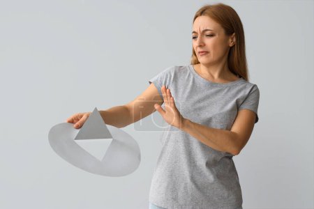 Mature woman rejecting paper thumbtack on light background. Hemorrhoids concept