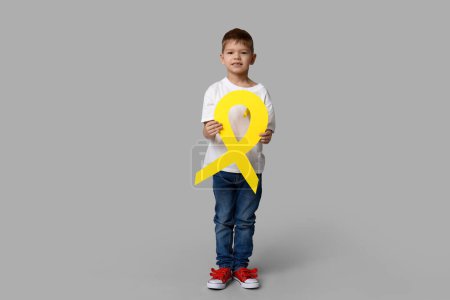 Téléchargez les photos : Joli petit garçon avec ruban jaune sur fond gris. Journée internationale du cancer chez les enfants - en image libre de droit