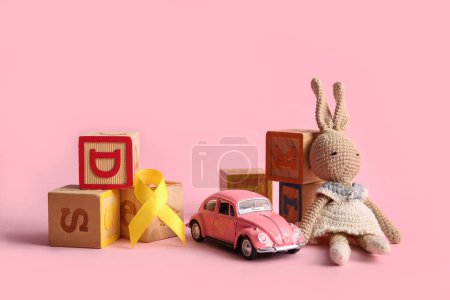 Téléchargez les photos : Ruban doré avec des jouets sur fond rose. Concept de sensibilisation au cancer chez les enfants - en image libre de droit