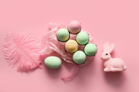 Téléchargez les photos : Support avec œufs de Pâques peints, plumes et lapin sur fond rose - en image libre de droit