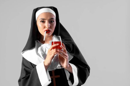Naughty nun with glass of wine smoking cigarette on light background