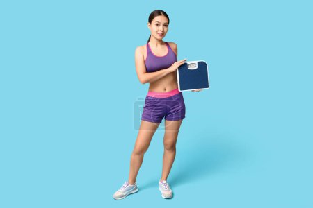 Photo for Young woman in sportswear and with weight scales on blue background. Slimming concept - Royalty Free Image