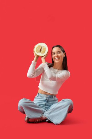 Foto de Mujer joven sonriente con la mitad de pomelo sentado sobre fondo rojo - Imagen libre de derechos
