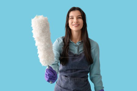 Young woman in apron with pp-duster on blue background