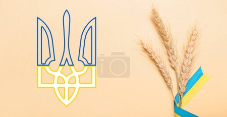 Wheat spikelets and ribbons in colors of Ukrainian flag with coat of arms on beige background