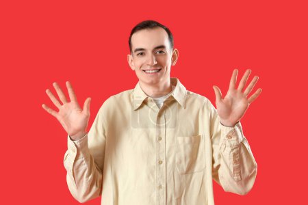 Téléchargez les photos : Jeune homme montrant dix doigts sur fond rouge - en image libre de droit