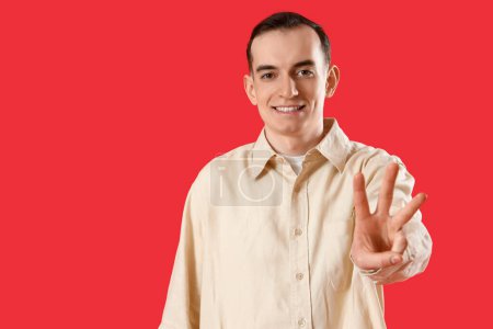 Téléchargez les photos : Jeune homme montrant trois doigts sur fond rouge - en image libre de droit