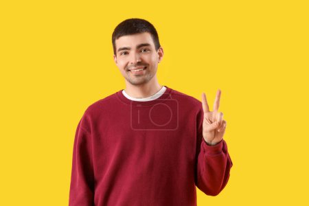 Téléchargez les photos : Jeune homme montrant geste de victoire sur fond jaune - en image libre de droit