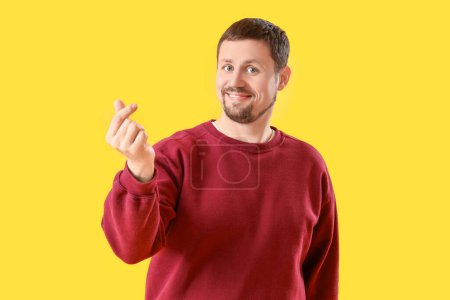 Photo for Handsome man making heart gesture on yellow background - Royalty Free Image
