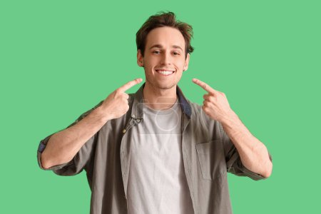 Téléchargez les photos : Jeune homme pointant son sourire sur fond vert - en image libre de droit