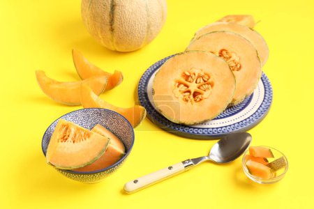 Teller und Schüssel mit süßen Melonenstücken auf gelbem Hintergrund