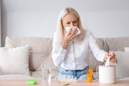 Mujer madura enferma con tejidos, pastillas y vaso de agua en casa