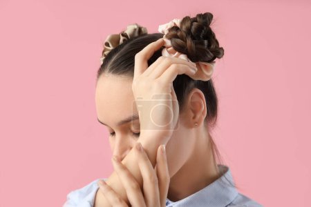 Beautiful young woman with buns hairstyle and silk scrunchy on pink background