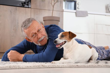 Foto de Hombre maduro con lindo Jack Russell terrier acostado en la alfombra en la cocina - Imagen libre de derechos