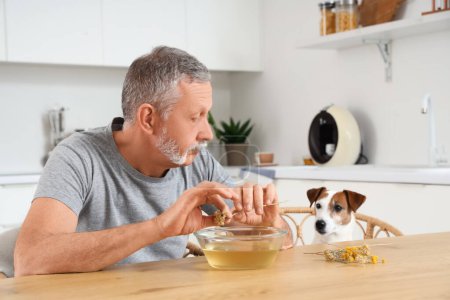 Mature man with dog preparing steam inhalation at table in kitchen