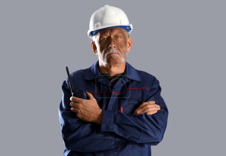 Mature miner man with two-way radio on grey background