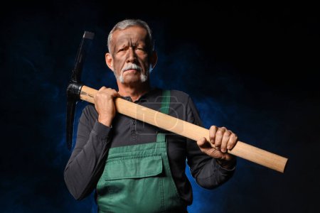 Photo for Mature miner man with pick axe and blue smoke on black background - Royalty Free Image