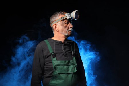 Mature miner man and blue smoke on black background