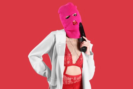 Beautiful young stylish woman in balaclava and sexy underwear with gun on red background